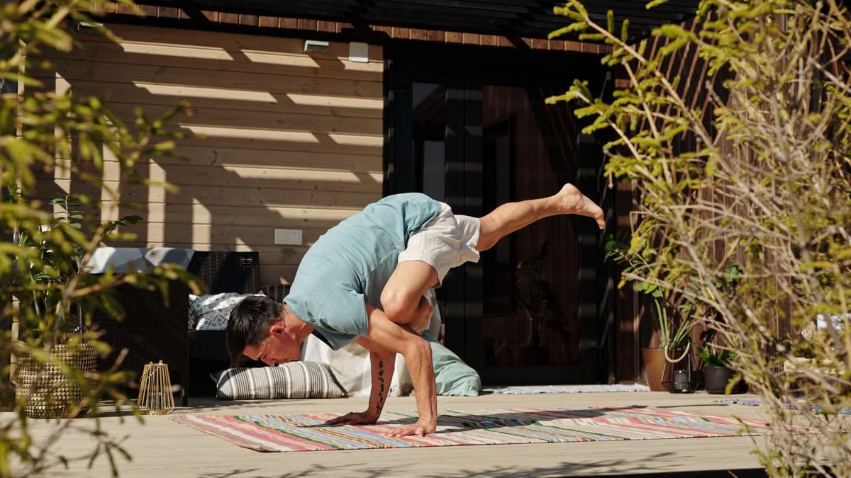 Man practicing yoga handstand balance pose on a sunny outdoor veranda.